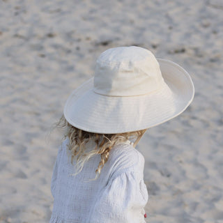 Young child facing the ocean, wearing Will & Bear Kids Packable Bucket Hat with brim covering neck and shoulders.