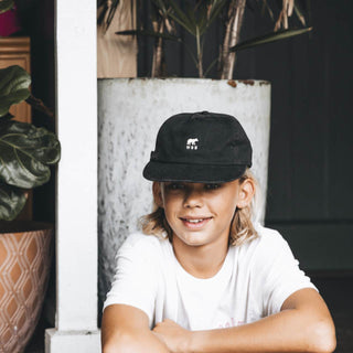 Smiling Child in Will & Bear Kids Black Cap – Indoor Portrait of Young Explorer in Soft Cotton Cap.