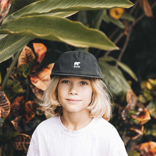 Young Child Wearing Will & Bear Kids Black Cap – Eco-Friendly Cap for Kids in Outdoor Setting.