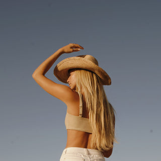 Woman wearing a straw cowboy hat and beige top against a clear blue sky