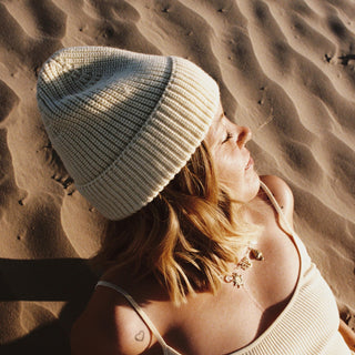 Woman wearing the Will & Bear Bambi Custard yellow wool beanie under the sun on sand dunes, perfect for cool adventures.