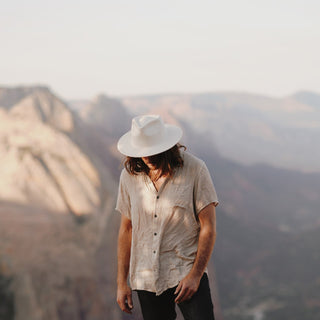 Man wearing the Will & Bear Calloway Bone white straw felt fedora with mountain scenery behind.