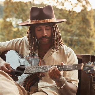 Man playing guitar outdoors with the Will & Bear Hat Scarf Hazel wrapped around his hat as a decorative band.