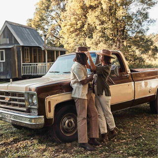Couple near a vintage truck, with the woman’s hat styled with the Will & Bear Hat Scarf Hazel wrapped around the crown.