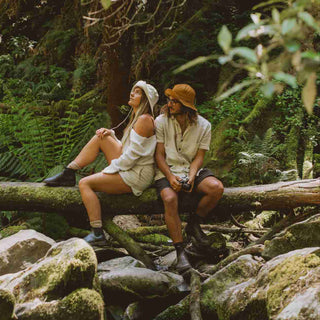 Couple sitting by a stream wearing Will & Bear Lenny Rust Orange Bucket Hats, styled for hiking and exploring.