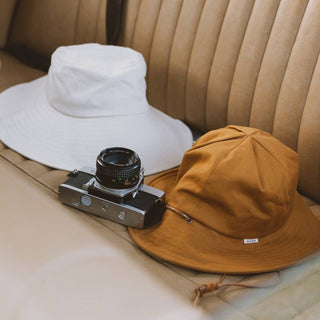 Two Will & Bear bucket hats including the Lenny Rust Orange Bucket Hat on a car seat, styled for travel.