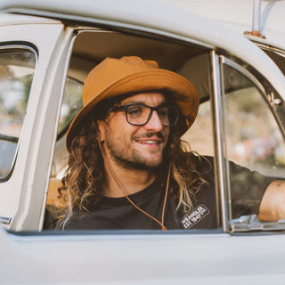 Man driving while wearing the Will & Bear Lenny Rust Orange Bucket Hat, relaxed road trip setting.