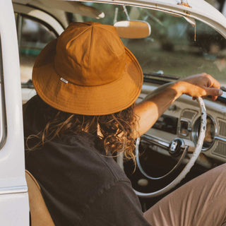 Man driving a vintage car while wearing the Will & Bear Lenny Rust Orange Bucket Hat, highlighting the relaxed fit, wide brim, and functional outdoor design.