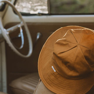 Will & Bear Lenny Rust Orange Bucket Hat resting on vintage car seat, perfect for travel and day trips.