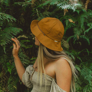 Woman wearing the Will & Bear Lenny Rust Orange Bucket Hat while exploring forest trails, styled for the outdoors.