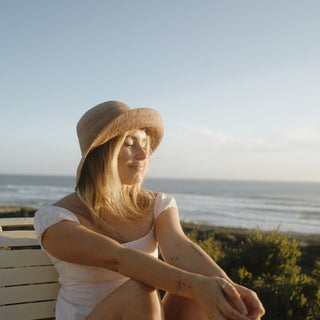 Woman wearing Will & Bear Women's Straw Bucket Hat, soaking up coastal sunset on grassy dunes