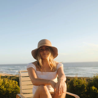 Woman relaxing on coastal bench in Will & Bear Women's Straw Bucket Hat, ideal for beach escapes