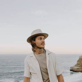 Man standing by the sea wearing Will & Bear William Cream white felt crushable fedora hat – perfect for travel and everyday adventure.