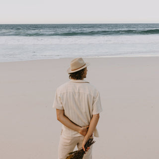 Back view of man walking on sand wearing Will & Bear William Cream white felt fedora hat – travel-ready and breathable.