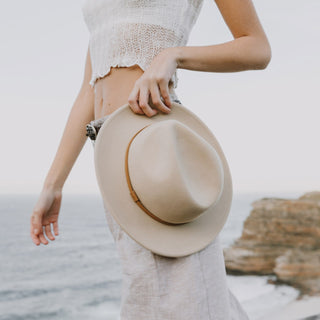 Woman holding Will & Bear William Cream white felt fedora hat at her side – natural tones made for sunny escapes.