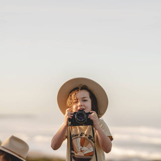Child holding camera and wearing Will & Bear Australian Wool Kids Fedora – Little Calloway Cream during golden hour.