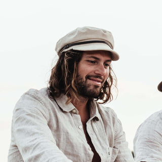 Man outdoors smiling in Will & Bear’s Baker Fawn cap, a white cord newsboy cap perfect for road trips.