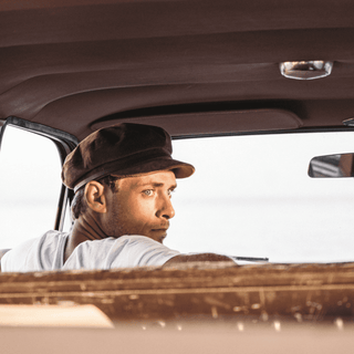 Man wearing the Will & Bear Baker Tan brown cord bakerboy cap driving a vintage car.
