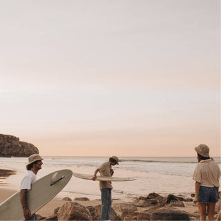 Friends Wearing Will & Bear Perry Bone Beige Cord Bucket Hats – Surfboards in Hand at Sunset Beach Gathering.