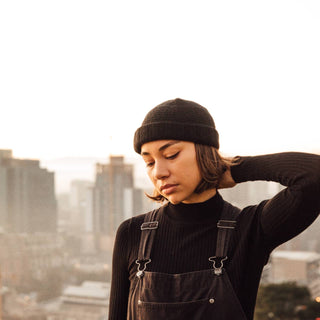 Woman wearing the Will & Bear Doc Black Wool Fisherman’s Beanie in an urban setting during golden hour.