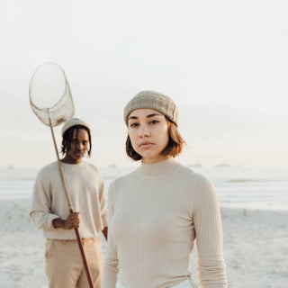 Woman wearing the Will & Bear Doc Fawn Wool Fisherman’s Beanie beside man holding fishing net on a windswept beach.