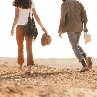Couple walking barefoot along the shoreline, both carrying Will & Bear hats including the Fischer Bone White Bucket Hat.