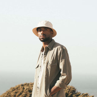 Man wearing the Will & Bear Fischer Bone White Bucket Hat outdoors by the coast, styled for warm-weather adventures.
