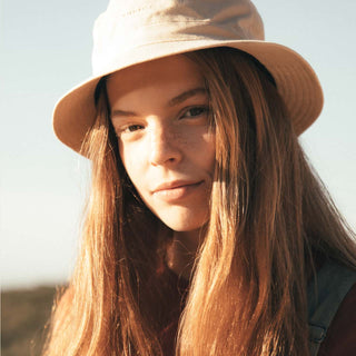 Woman in the Will & Bear Fischer Bone White Bucket Hat standing outdoors in soft light with natural hair styling.