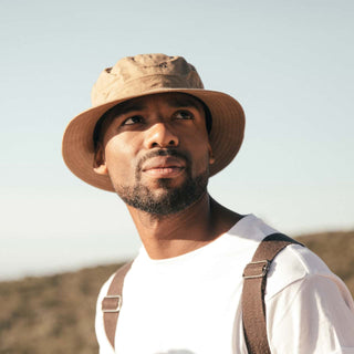 Man looking toward the sun wearing the Will & Bear Fischer Sand Waxed Canvas Bucket Hat with backpack straps visible.