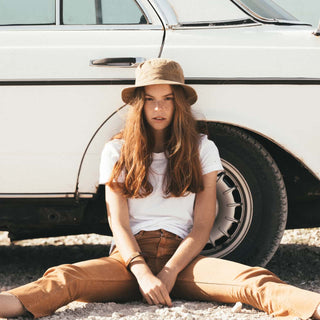 Woman wearing the Will & Bear Fischer Sand Waxed Canvas Bucket Hat sitting next to a classic white car.