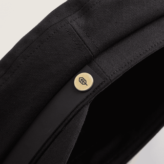 Close-up detail of Will & Bear Foster Black Newsboy Cap, showing branded metal button and premium finish.