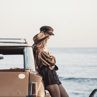 Man leaning on a vintage vehicle wearing the Will & Bear Foster Black Newsboy Cap, ocean in background.