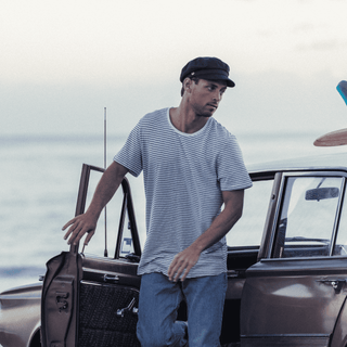Man standing by a vintage vehicle at the beach wearing the Will & Bear Foster Black Newsboy Cap.