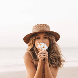 Woman holding daisies while wearing the Will & Bear Harvey Amber Women’s Straw Boater, styled for summer.