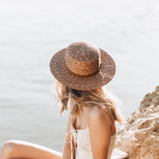 Woman sitting on a rock overlooking the sea, wearing the Will & Bear Harvey Amber Women’s Straw Boater.