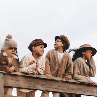 Group of children wearing Will & Bear Kids Newsboy Cap – Little Baker Tan leaning on a wooden railing.