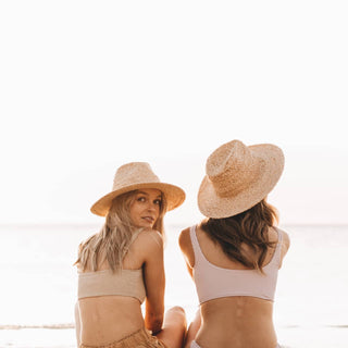 Two women wearing Will & Bear Men's and Women's Straw Hats, relaxing on the beach at sunset