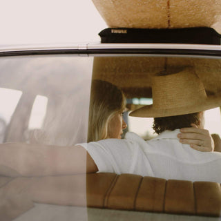 Couple sharing a moment in the back seat with Will & Bear Wide Brim Straw Hat – Sawyer Sand – overhead storage shot.