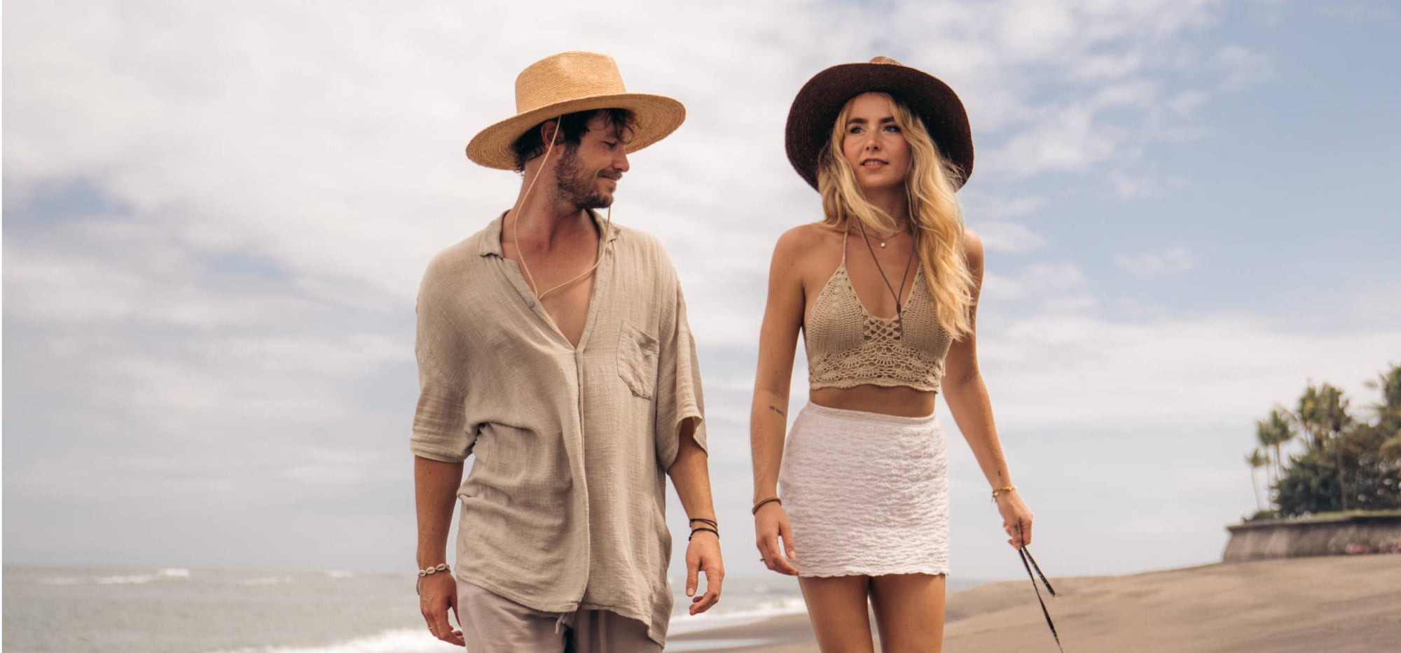 Man and woman wearing wide brim sun hats walking along the beach
