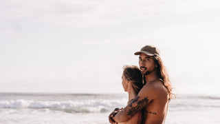 Man and woman at the beach hugging and the man wearing a mens Will & Bear cap