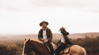 Two riders in the outback, donning Akubra style hats, share a journey on horseback across the plains.