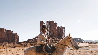 A rider in a western hat sits astride a horse, with majestic rock formations in the background.