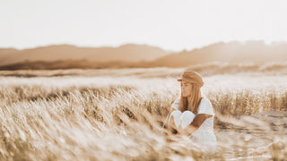 Woman sitting at the beach at sunset wearing a vintage baker cap by Will & Bear