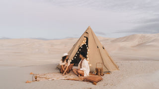 Two women chat by a tent in the dunes, both sporting Will & Bear camping hats.