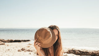 A woman on a sunny beach day peers through her crushable travel hat by Will &Bear, enjoying the coastal vibe