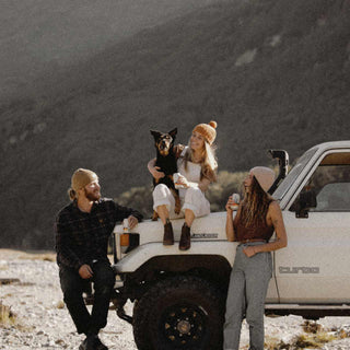 Group of people sitting on a car with a dog wearing Australian wool beanies