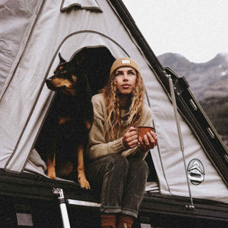 Woman sitting in tent with dog wearing a beanie