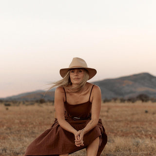 Woman seated in open landscape wearing Anderson Cream hat and linen jumpsuit