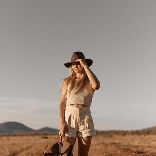 Woman walking in sunlit field wearing Anderson Olive fedora and linen outfit