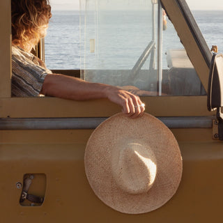 Person holding rustic wide brim straw hat on road trip